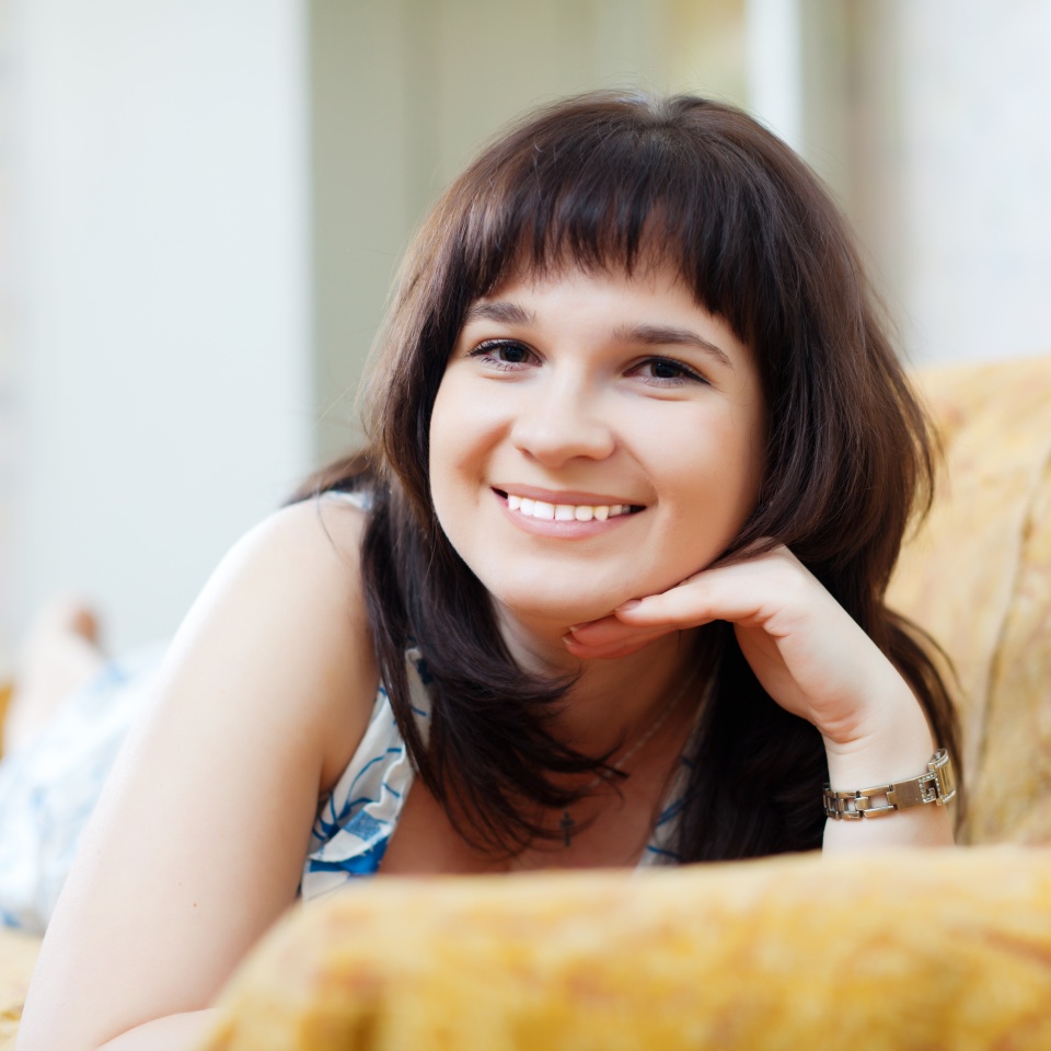 Smiling ordinary woman lying on couch at home