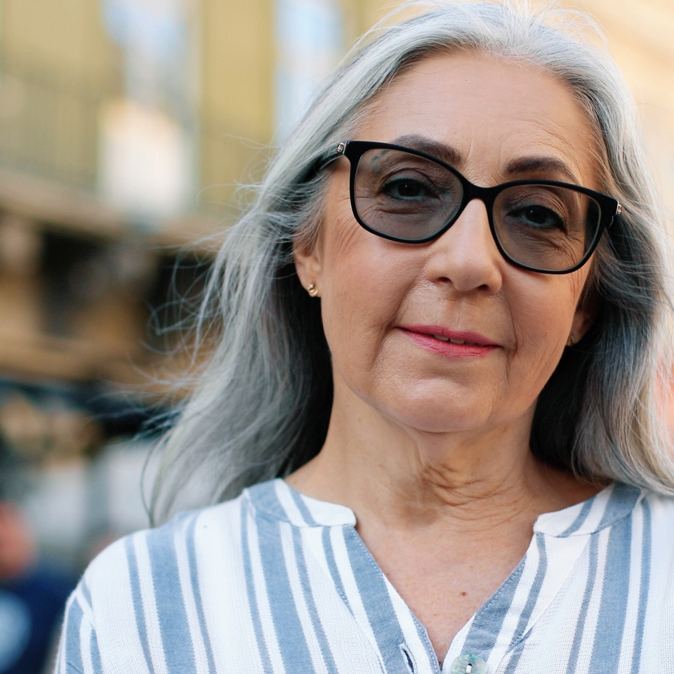 Portrait view of the calm mature woman enjoying of the fresh air and smiling to the camera while walking alone through the summer street. People lifestyle concept