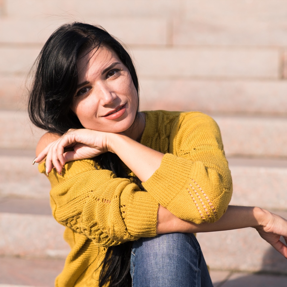 Beautiful and attractive caucasian brunette girl in a yellow sweater posing while sitting on the steps.