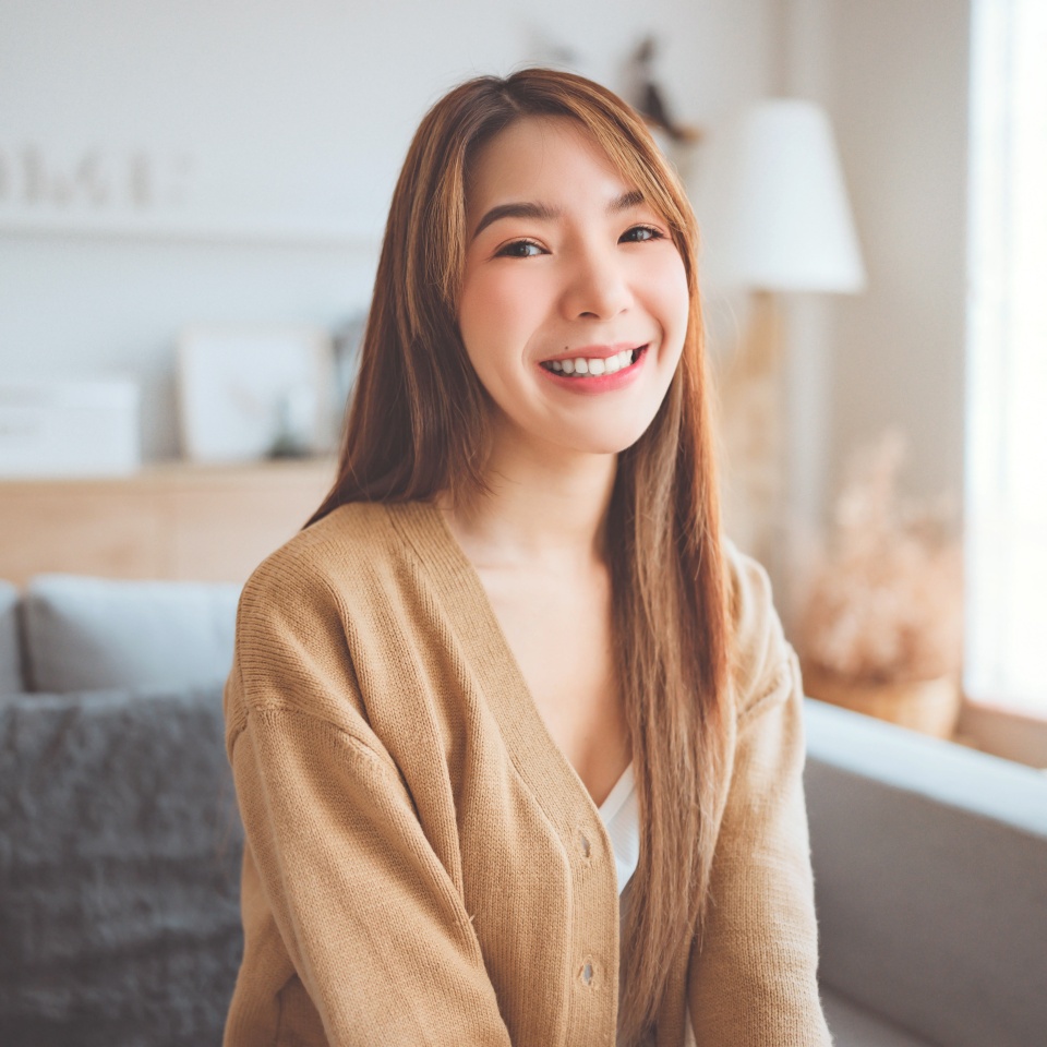 Confident smiling young adult asian woman looking at camera while sitting at home, Happy beautiful lady pretty face dental smile posing alone indoors.