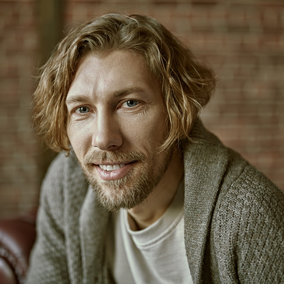 Portrait of a handsome forty-year-old man with curly hair, dressed in a casual knitted cardigan, who looks happily to the camera. Loft interior. Life style. People, emotions.