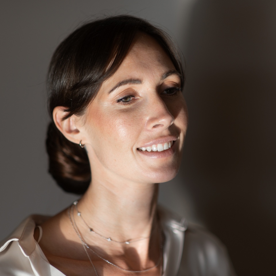 A calm smiling woman standing against a gray wall in the sunlight