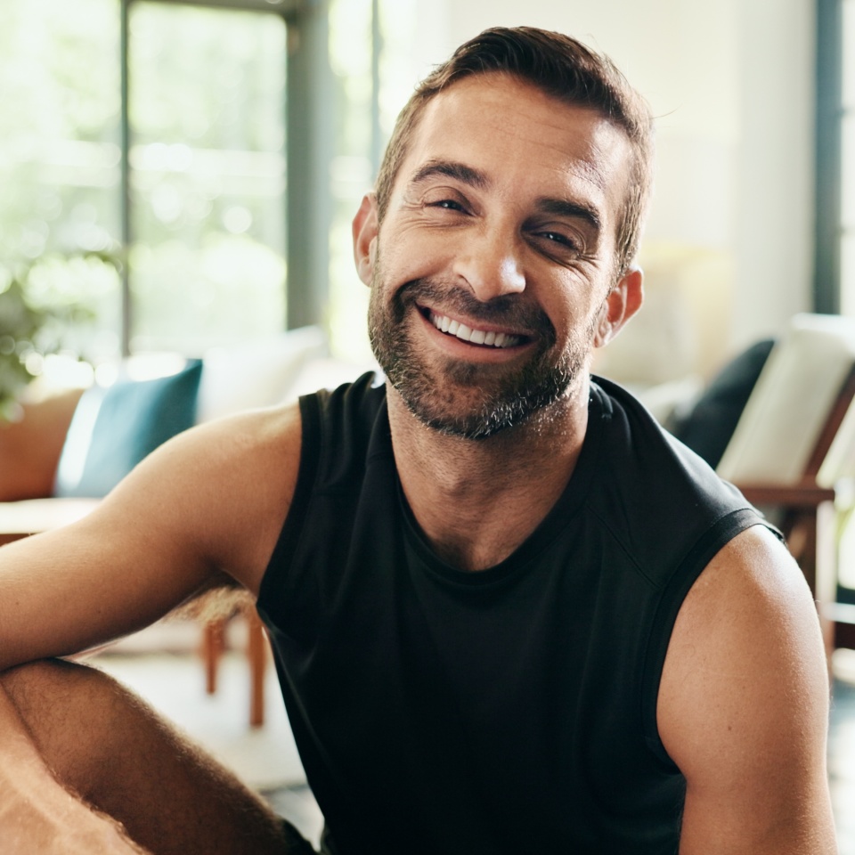 Portrait, happy and man in living room, fitness and healthy in home, exercise and athlete with sportswear. Morning, routine and person on break for workout, wellness and smile in lounge in Canada