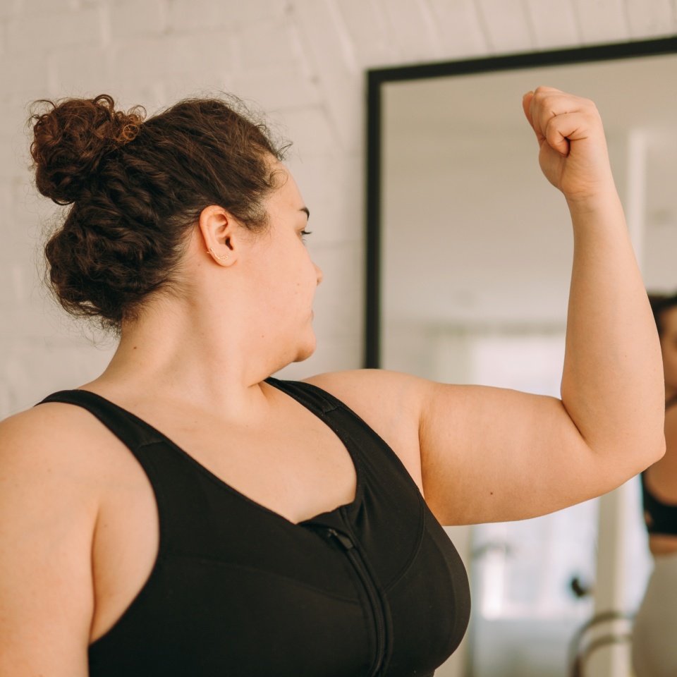 An overweight young woman in sportswear looks at herself and her hands in the mirror.Healthy lifestyle.