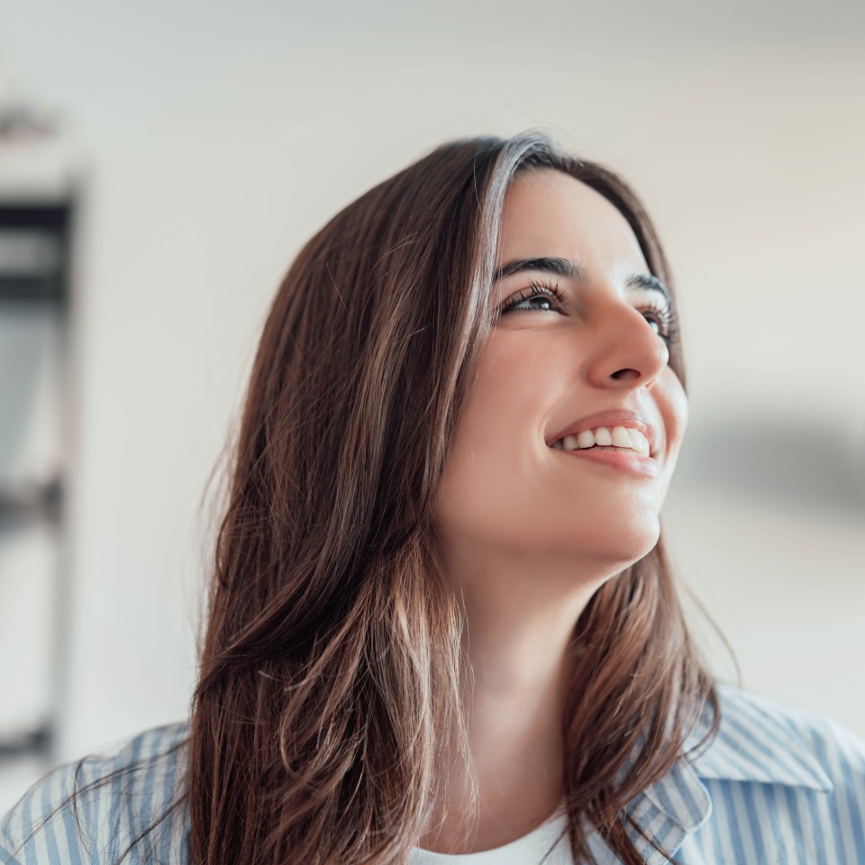 One young happy and cheerful woman smiling and dreaming alone at home looking up imagining her desires. Brunette female relaxing peaceful at home