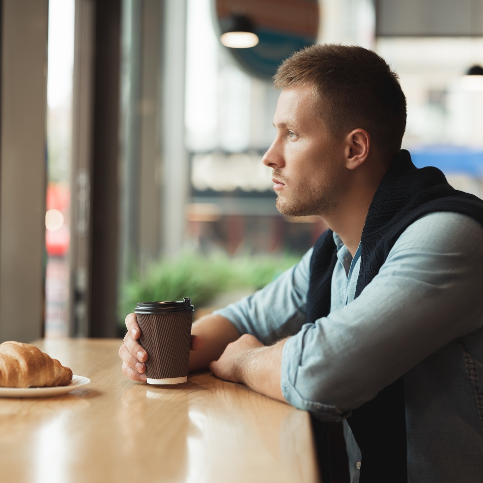 young handsome man having his croissant and drinking hot coffee for lunch in the cafe