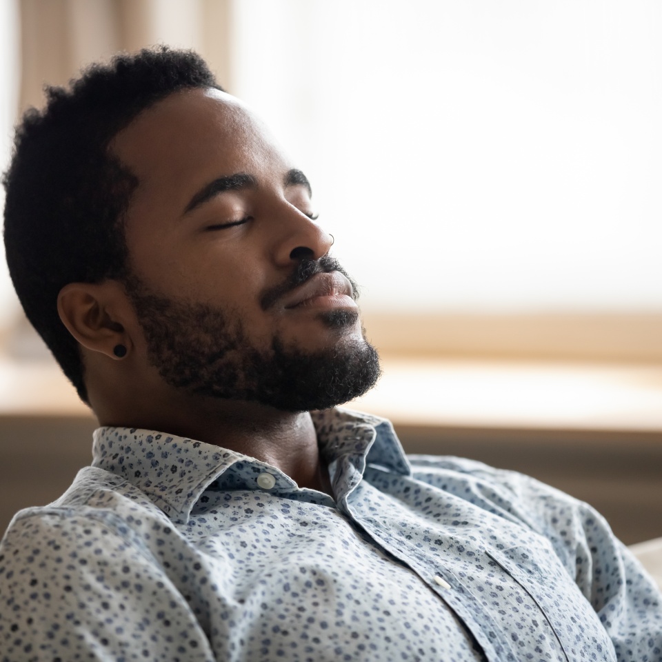 Tranquil calm young african american man resting with eyes closed taking deep breath of fresh air enjoy comfort relaxing on couch feel peace mind and stress relief meditate at quiet home sit on sofa