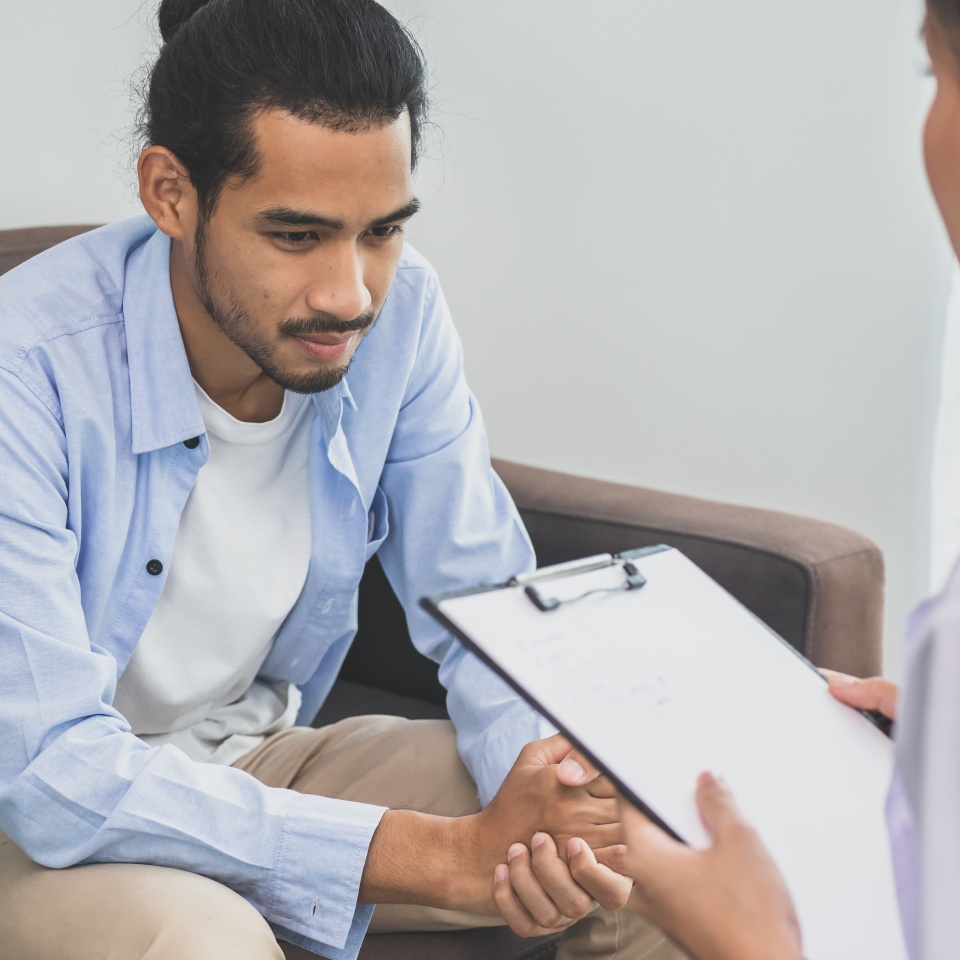 Asian young asian man, male has mental symptoms which must have been therapy and stress, sitting on couch to consult to psychologist during the session take notes to find out how to treat therapist.