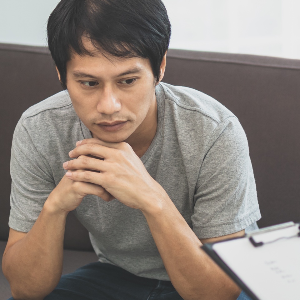 Asian young man, male has mental symptoms which must have been therapy and stress, sitting on couch to consult with psychologist during session taking notes to find out how to treat therapist.