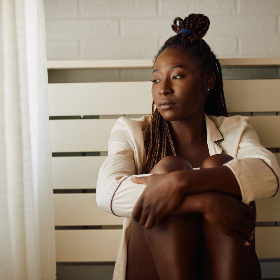 Young African American woman feeling sad and thinking of something while looking through the window at home. Copy space.