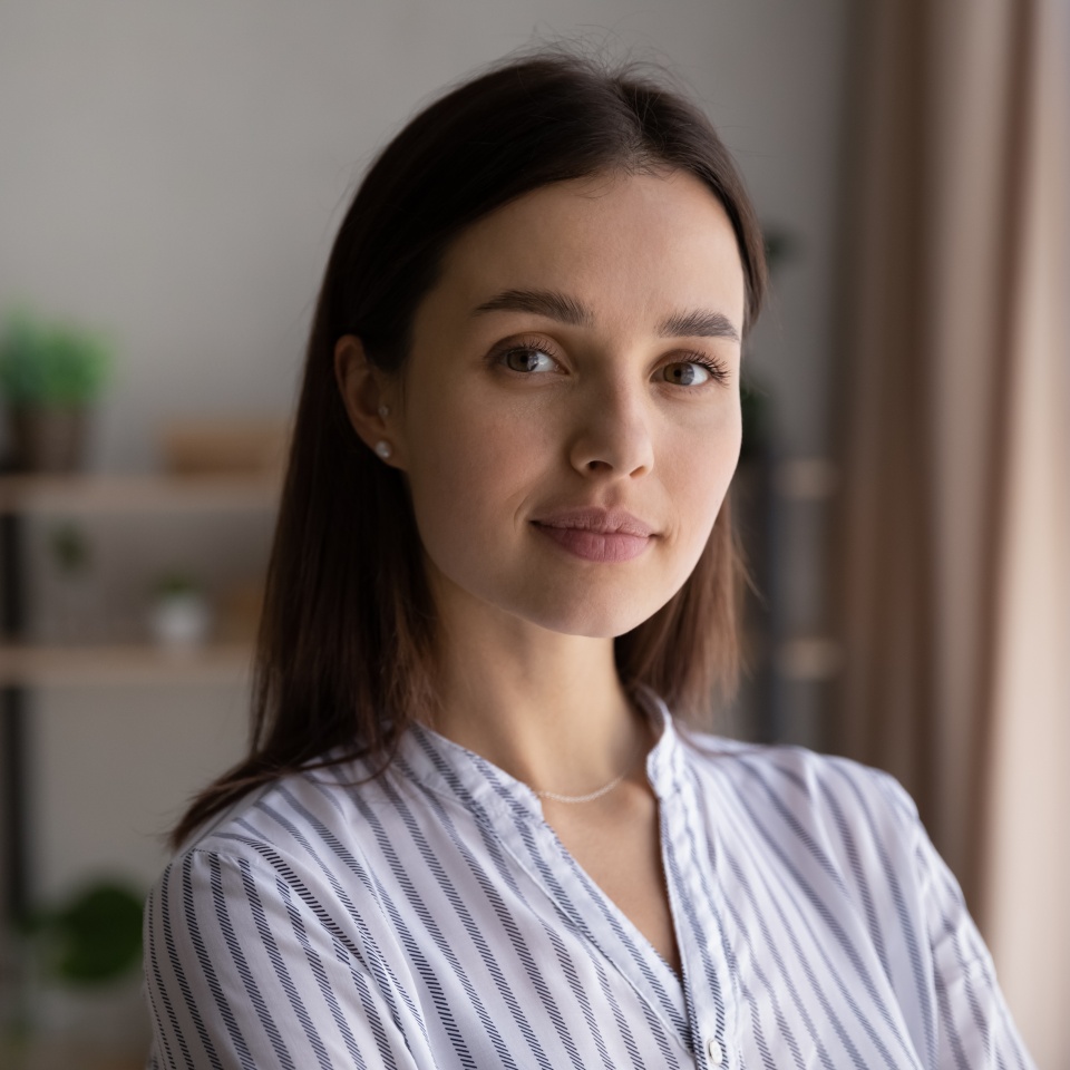 Close up head shot portrait of smiling beautiful young 30s dreamy woman posing at home. Happy pleasant millennial generation lady with perfect skin looking at camera, feeling confident indoors.