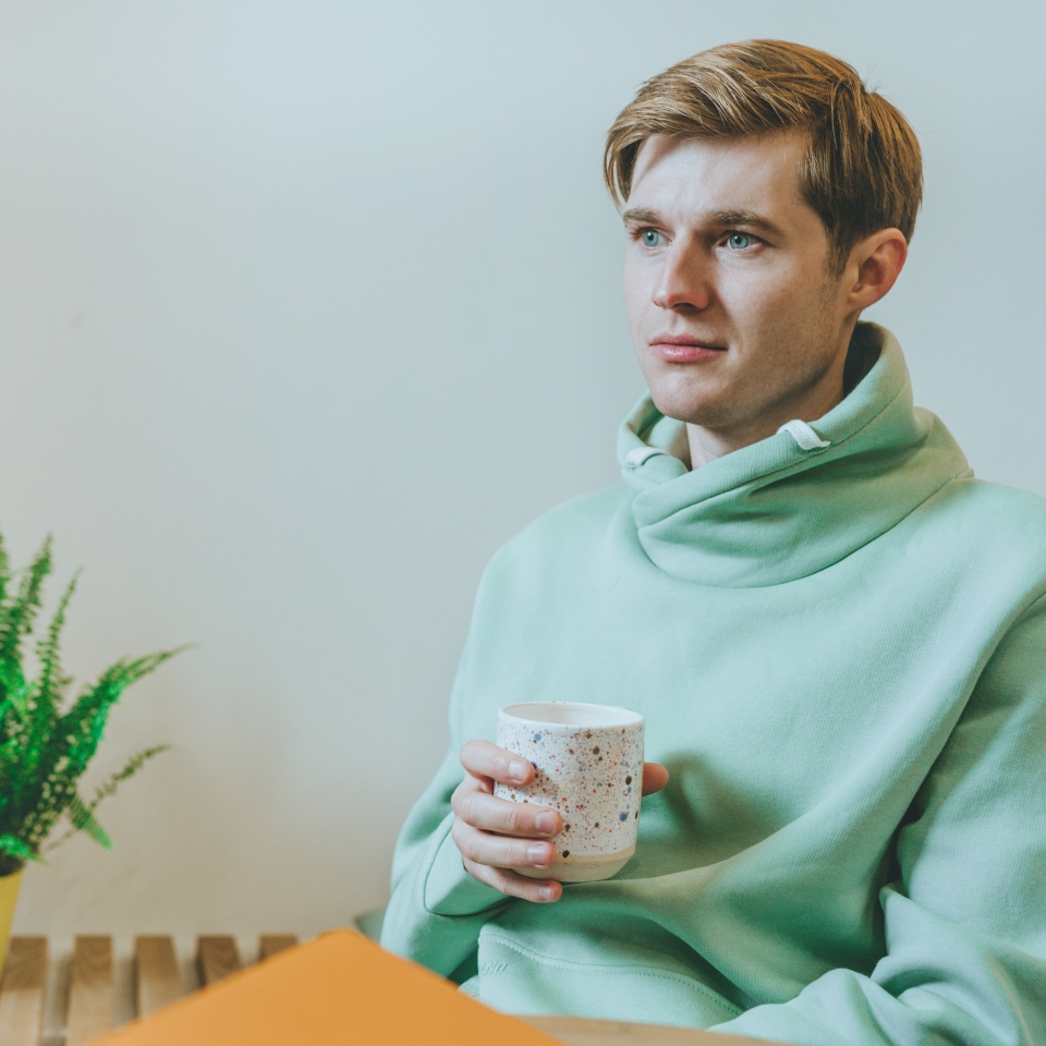 Thoughtful young man sitting in the cafe with cup of coffee looking at the window. Selective focus.