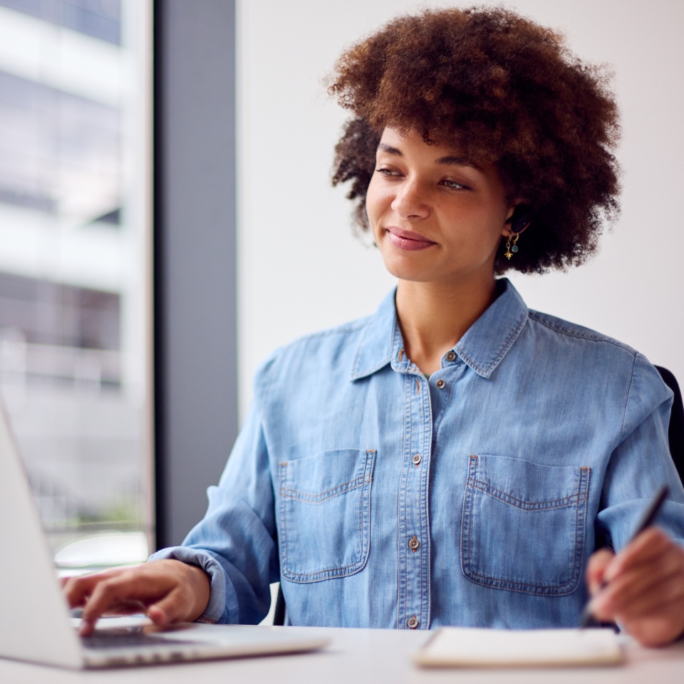 Young Businesswoman In Modern Office Working On Laptop Using Wireless Earpiece