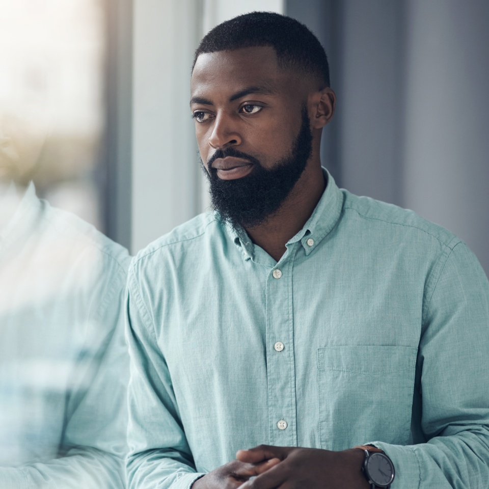 Idea, window and a business black man thinking or planning in his professional office at work. Flare, problem solving and decision with a serious young male employee standing alone in the workplace