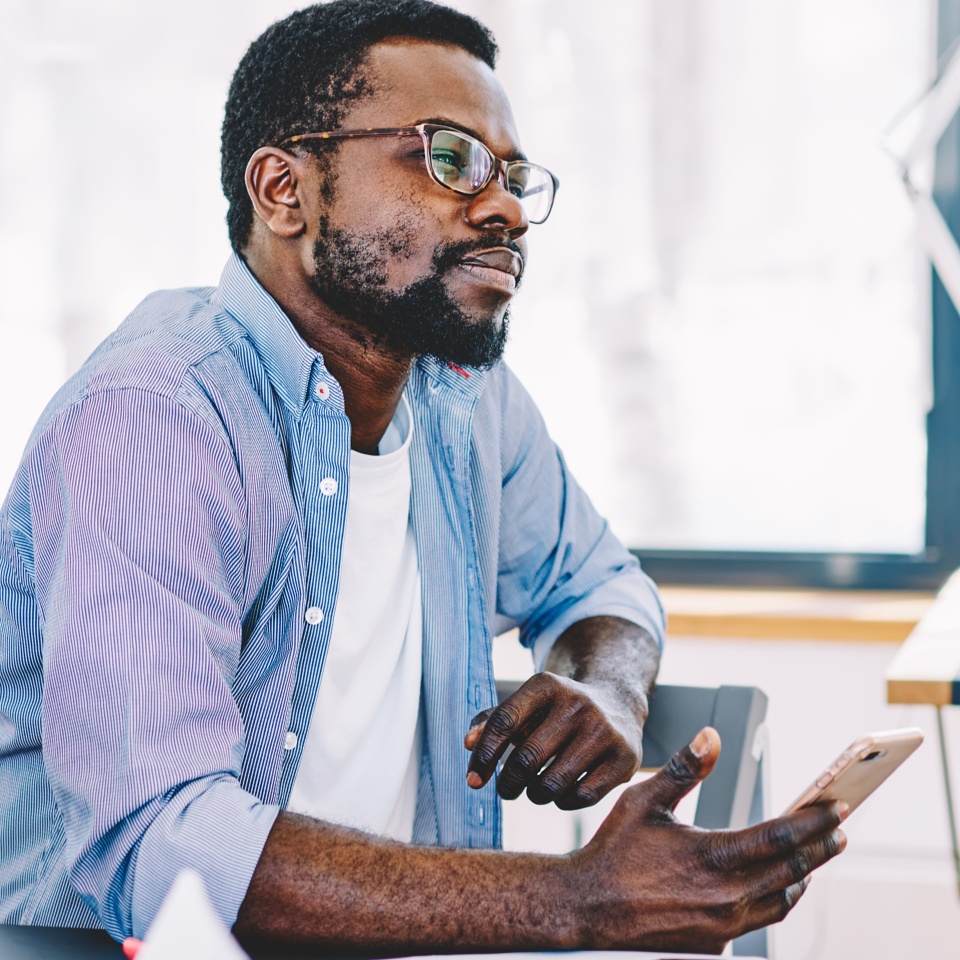 Thoughtful black man with smartphone sitting in office