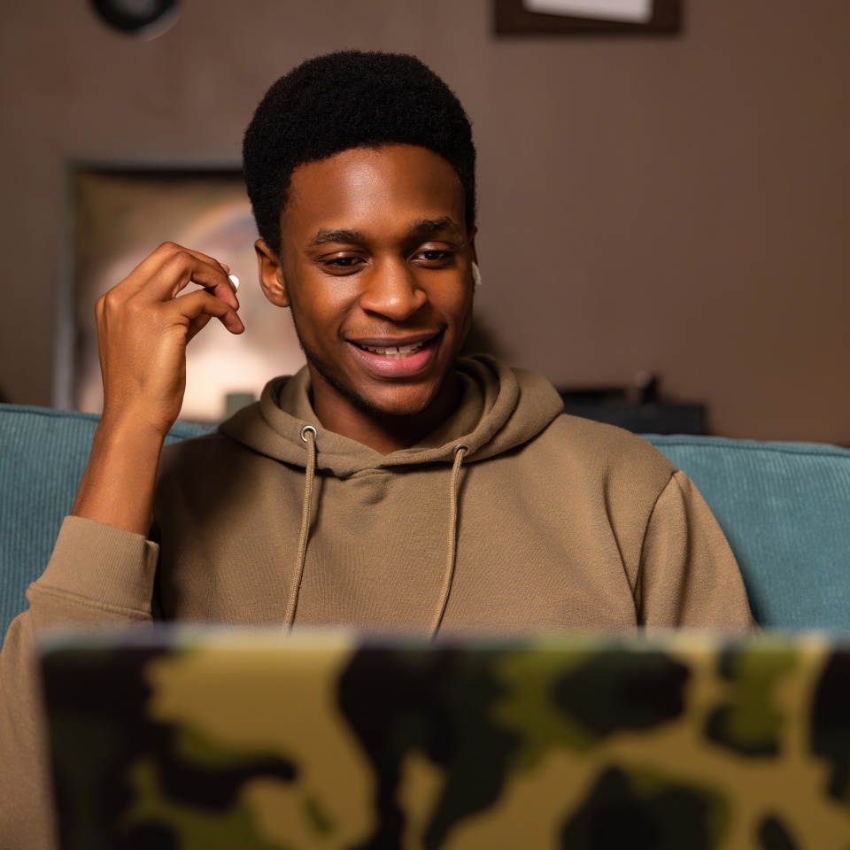 Happy black male student at cozy home watching a movie or TV show on his laptop, using the headphones to block out background noise and fully immerse himself in the content.
