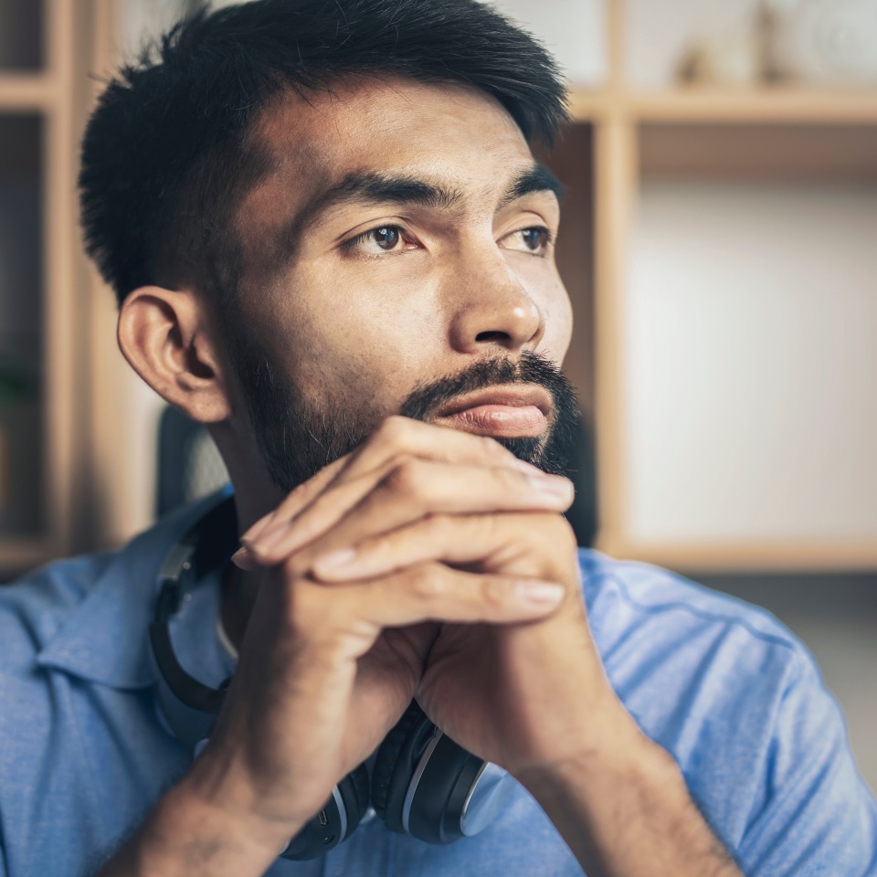 Thoughtful young bearded man sad looking out window while sitting on desk at home office