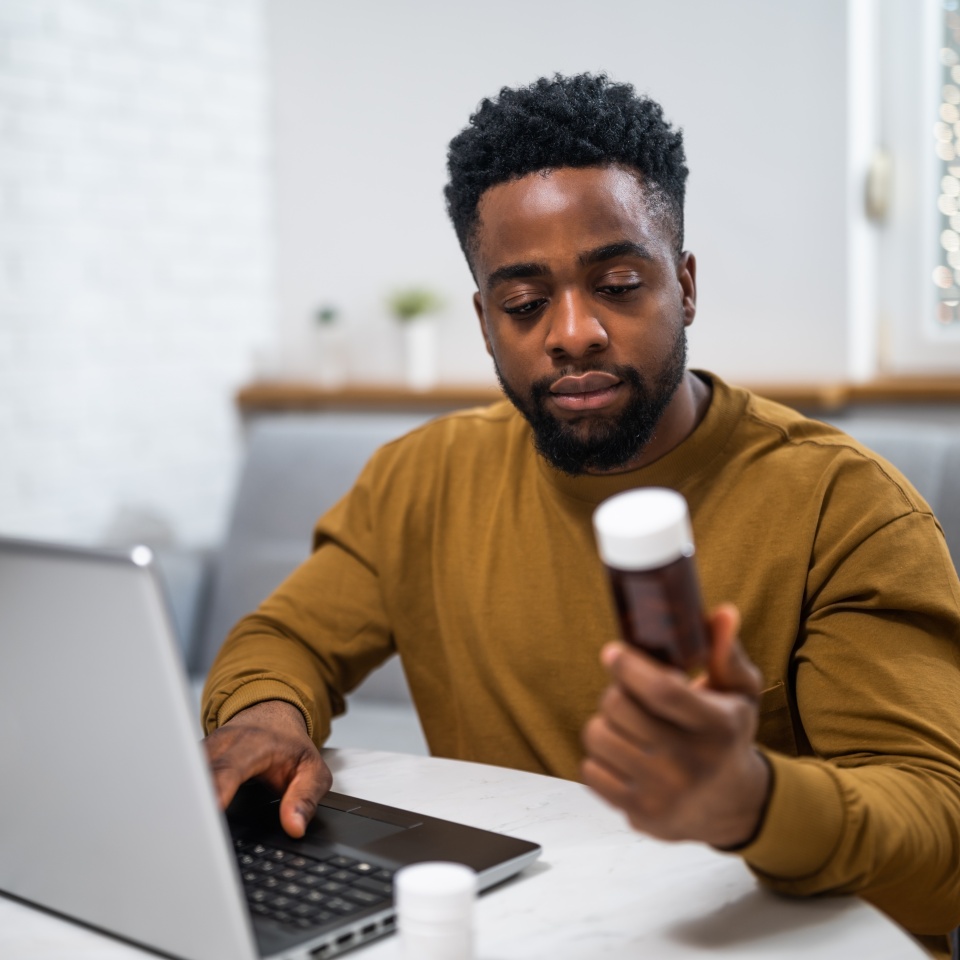 Young man using laptop for searching details about his prescribed medication while sitting at his cozy home.